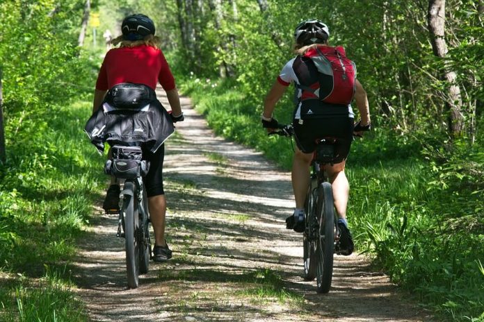 dvije ženske osobe voze bicikl u šumi